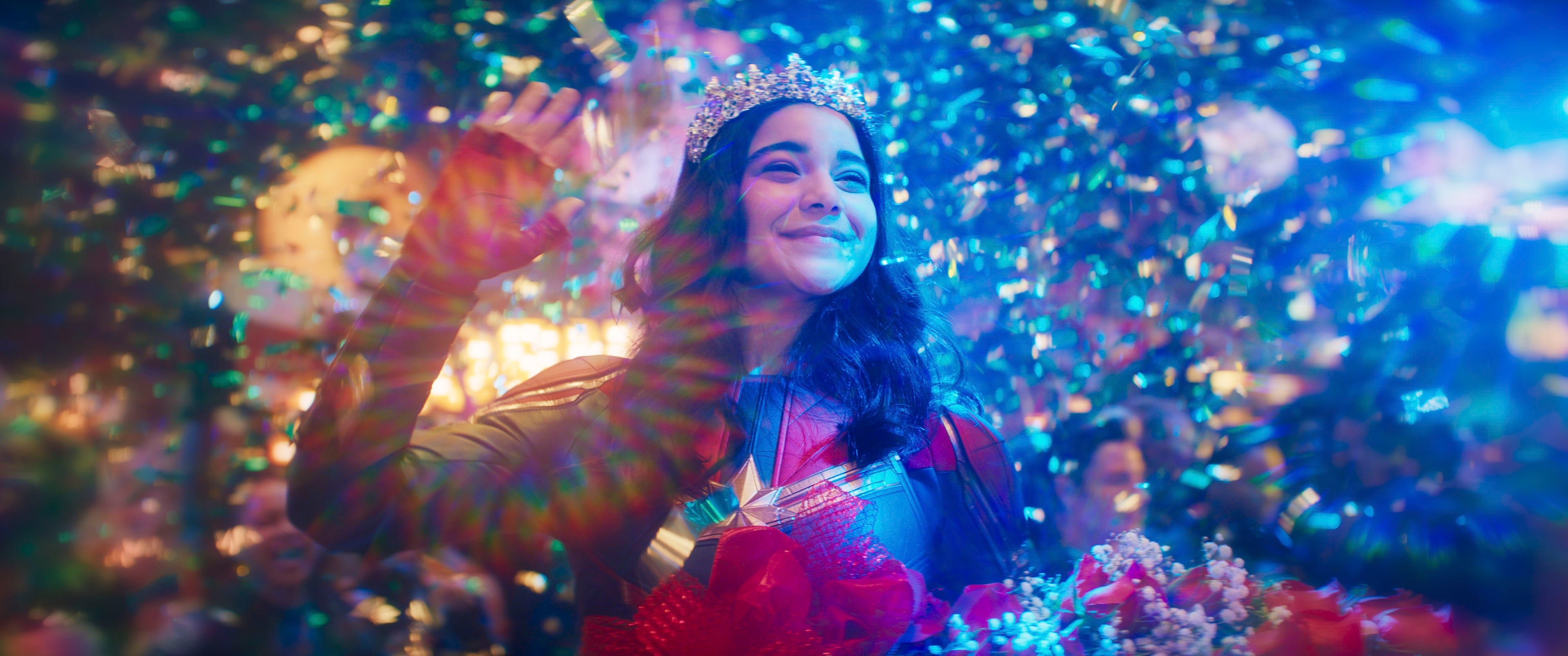 Ms. Marvel still Iman Vellani as Kamala Khan wearing a Tiara and waving whilst surrounded by confetti