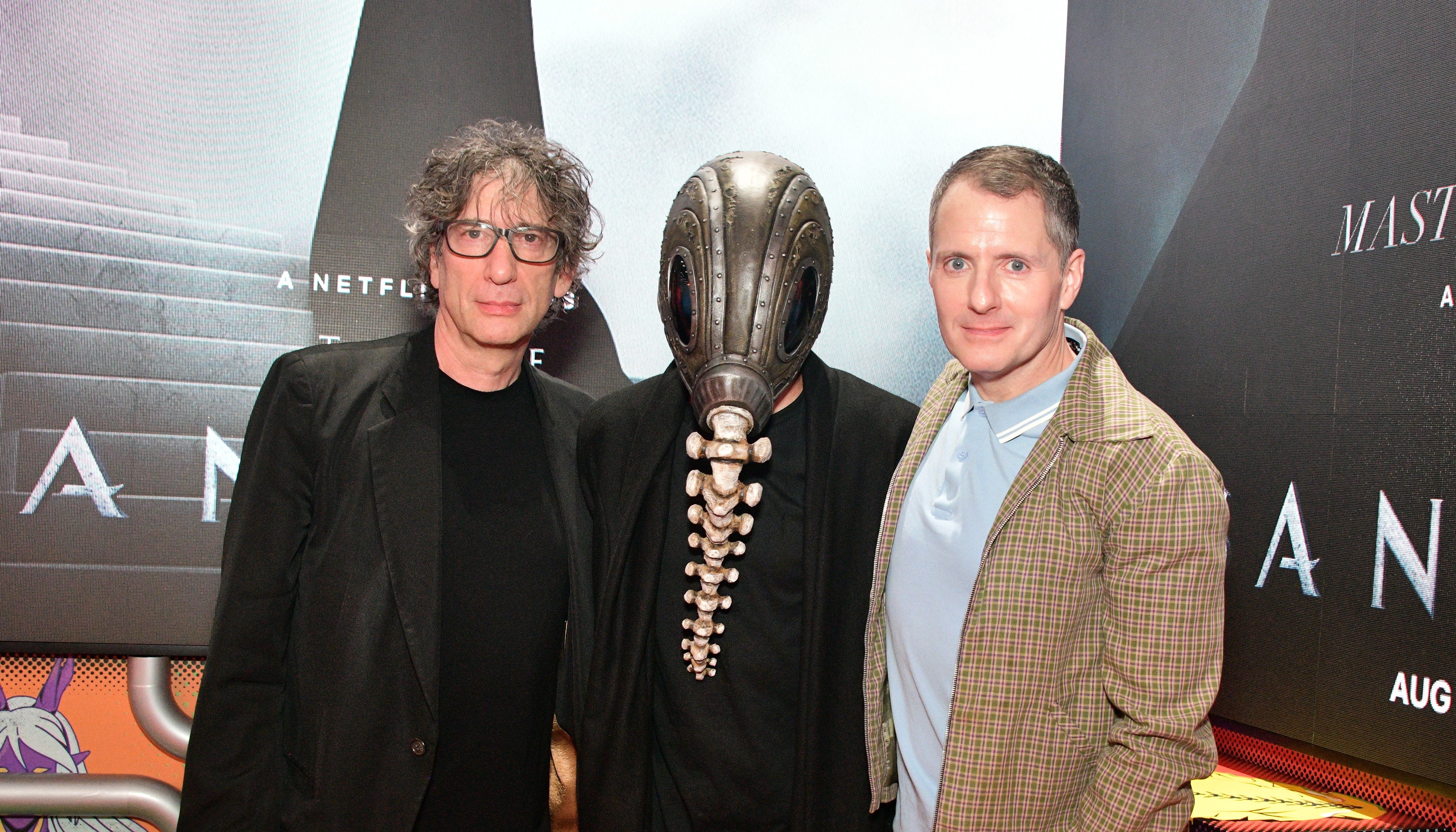 Image of Neil Gaiman and Allan Heinberg with masked figure at Sandman Press event