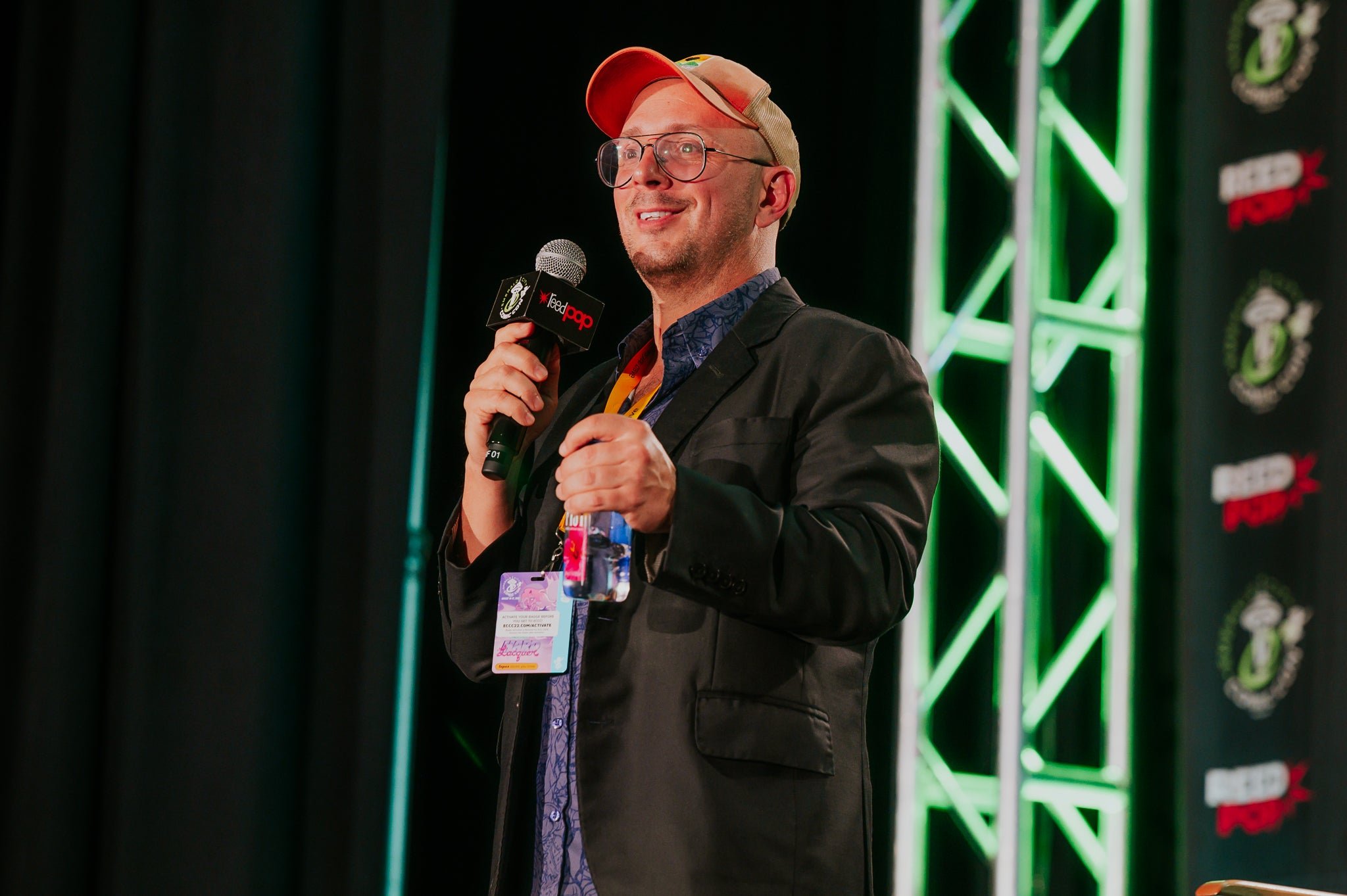 Steve Burns wearing a cap, glasses, and holding a microphone on stage