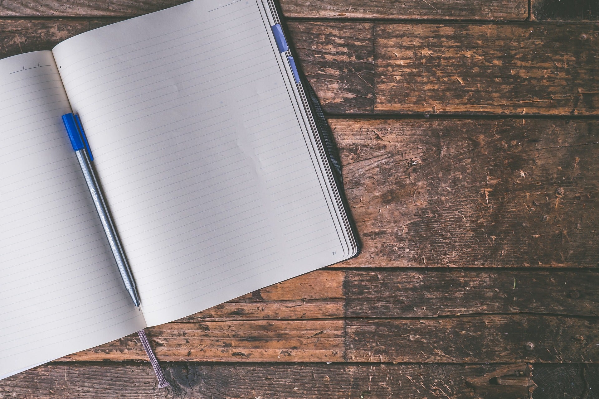 Photograph of an open notebook and blue pen on a dark wood desk