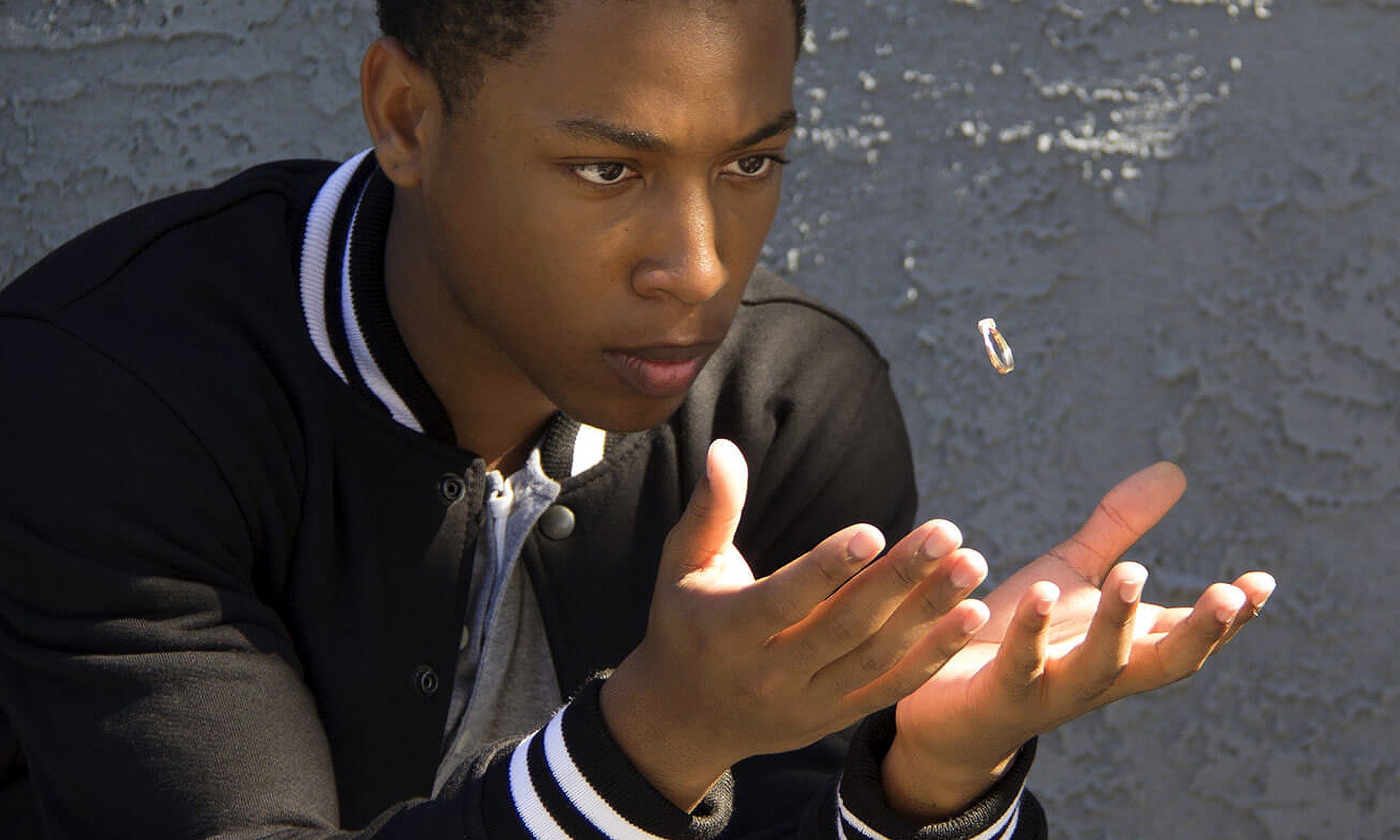 Still movie image featuring a young man in a black jacket and white trim. He is looking at a small item levitating above his open hands