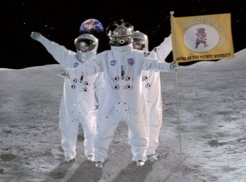 Three figures in astronaut suits, one holding a flag on the moon with the Earth in the background
